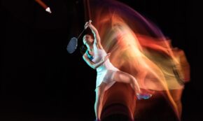 Young woman playing badminton isolated on black background in mixed light. Female model with the racket in action, motion in game with the fire shadows. Concept of sport, movement, healthy lifestyle.