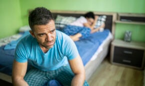 Couple having relationship trouble: the man sits at the end of the bed wondering what he did wrong.