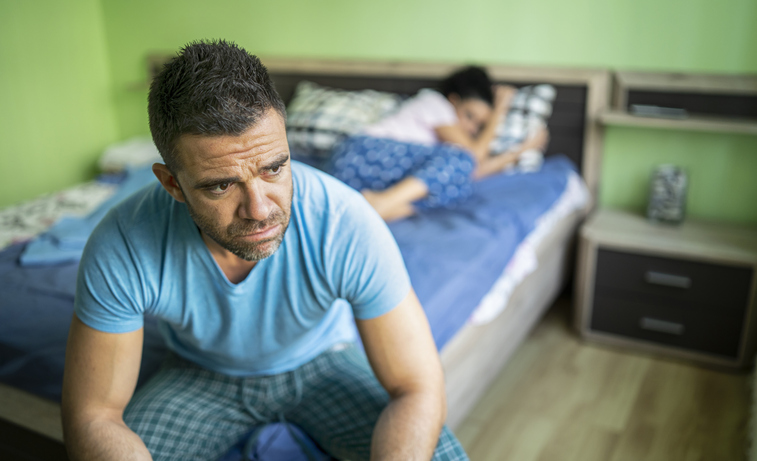 Couple having relationship trouble: the man sits at the end of the bed wondering what he did wrong.
