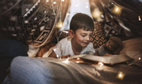 Cropped shot of an adorable young boy reading a storybook while lying in his blanket fort