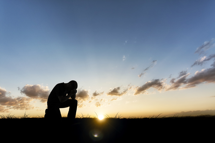 A man bows to his knees as the sun rises behind him.