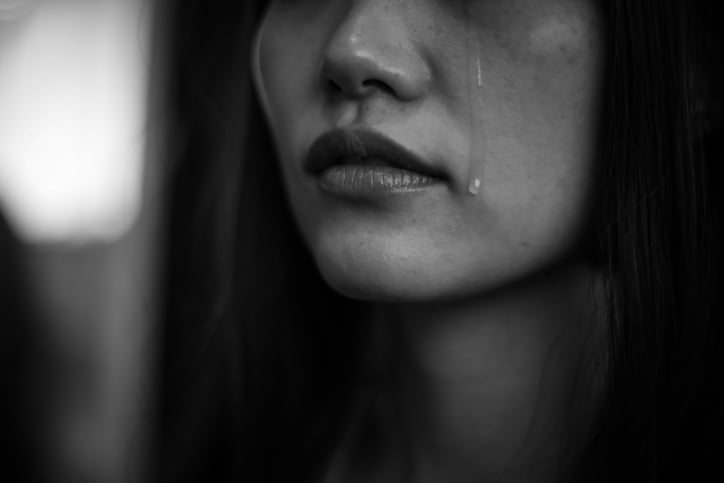 Black and white image of a young woman's face below the eyes, showing a tear streaming down her cheek.
