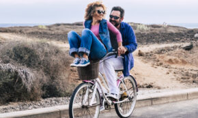 Young couple having fun in outdoor road leisure activity together - young couple going for a bike ride on a autumn day in the city - man carry woman and both laugh and enjoy lifestyle and love