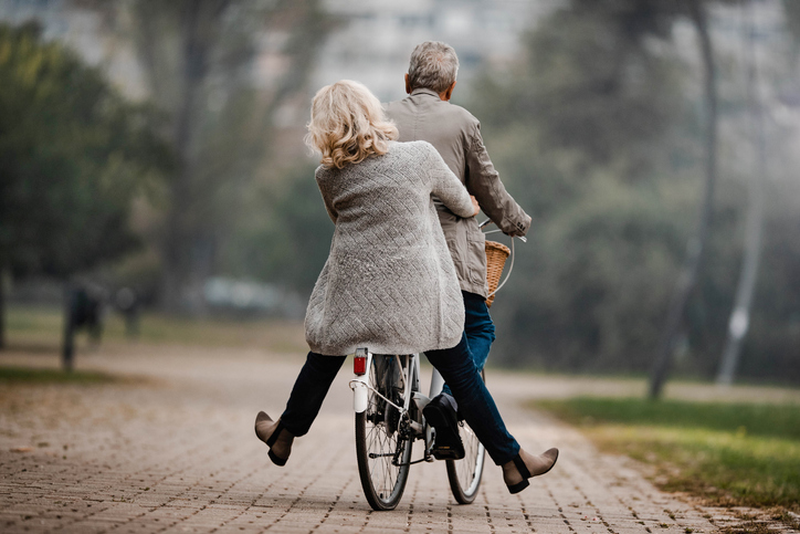 Back view of mature couple having fun on a bicycle in autumn day at the park. Copy space.