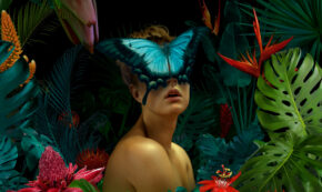 Surrealist painting of a woman in a field of oversized flowers, her face covered by an enormous Emperor butterfly.