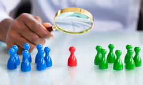 Unidentified person examining a red pawn in between two groups of pawns, one blue and one green.
