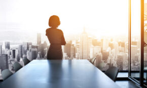 Rearview shot of a young businesswoman looking out from a large window in the office.