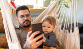 Unfocused Stay-at-home dad on smartphone ignoring child.