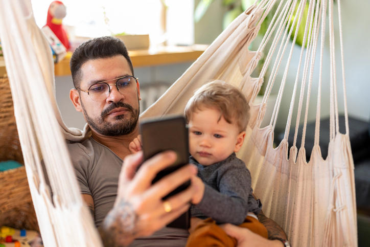 Unfocused Stay-at-home dad on smartphone ignoring child.