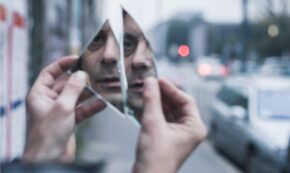 Man looking at his reflection in the pieces of a broken mirror.