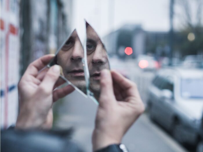 Man looking at his reflection in the pieces of a broken mirror.