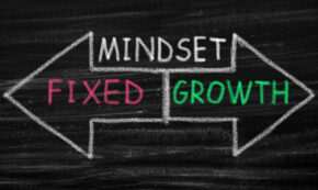 Two arrows drawn in chalk, pointing in opposite directions. A label above them reads the word "Mindset" and the arrow pointing to the left reads "Fixed" while the right arrow reads "Growth."