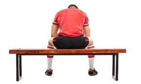 Sad football player sitting on a wooden bench