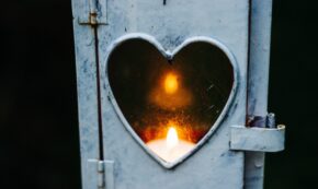 photo shows a lit votive candle inside an old style, whitewashed light box that has a heart-shaped glass pane.