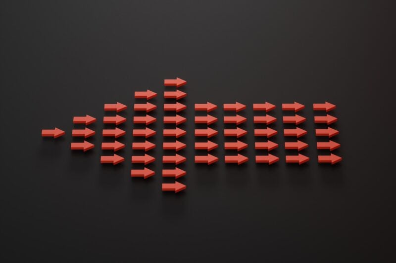 A group of 50 red arrows, individually pointing to the right, collectively form a single large arrow that is pointing to the left. The background is black. The arrows are arranged in 10 columns as follows, center to the horizontal middle of the photo: 1, 3, 5, 7, 9, 5, 5, 5, 5, 5,