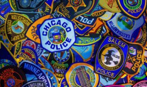 Photo shows several dozen police patches (such as those to be worn on a uniform shirt or jacket), each from a different municipality, with Chicago Police and Salem Police being prominently displayed. The photo is very colorful with the entire height and width being full of patches.