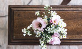 Image shows the top-down view of a closed casket with a bouquet of pink and white flowers.