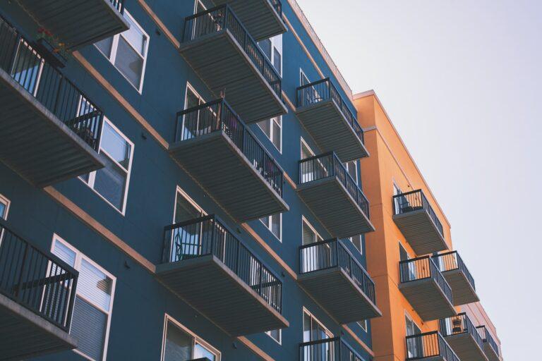 Filling the image frame is a low-angle view of two connected apartment buildings, the left of which is blue, and the right of which is orange. The photo was shot in Downtown, Raleigh, United States.