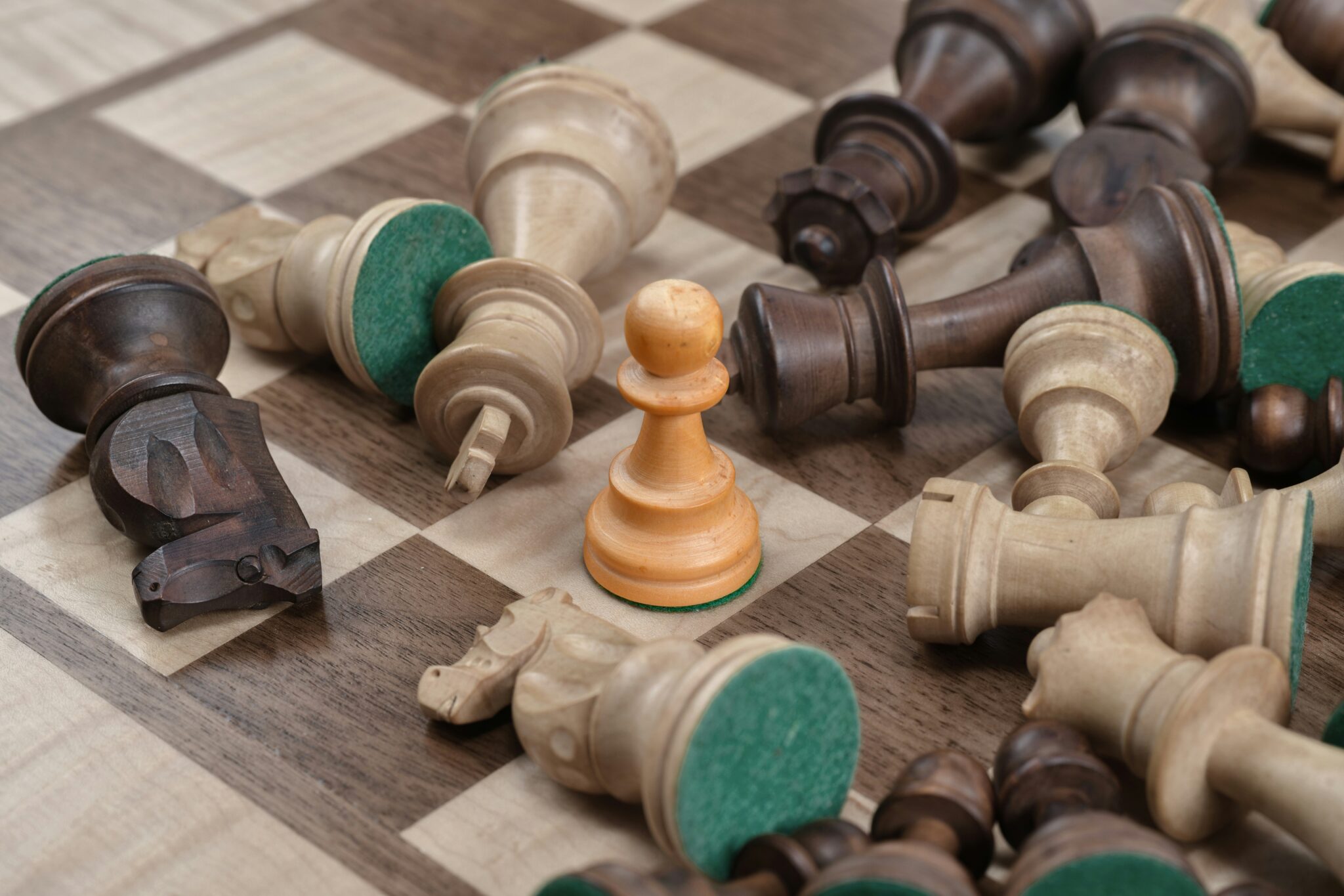 Image shows a close-up of chess pieces on a chess board. All pieces are knocked over except for one pawn.