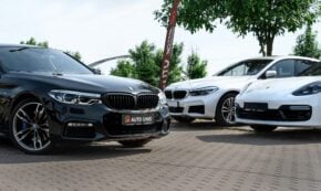 Close-up of three new cars parked in a dealer's outdoor lot with a tree in the background
