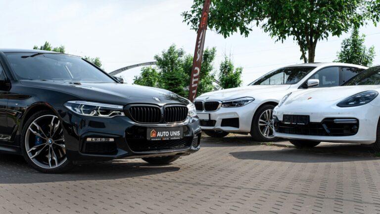 Close-up of three new cars parked in a dealer's outdoor lot with a tree in the background
