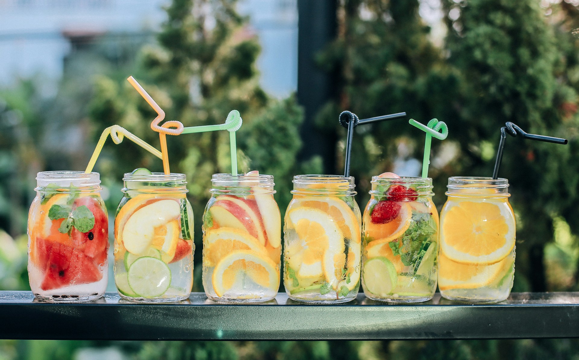 Image shows six Mason jars used to contain fruity beverages at a backyard bar in the summer.